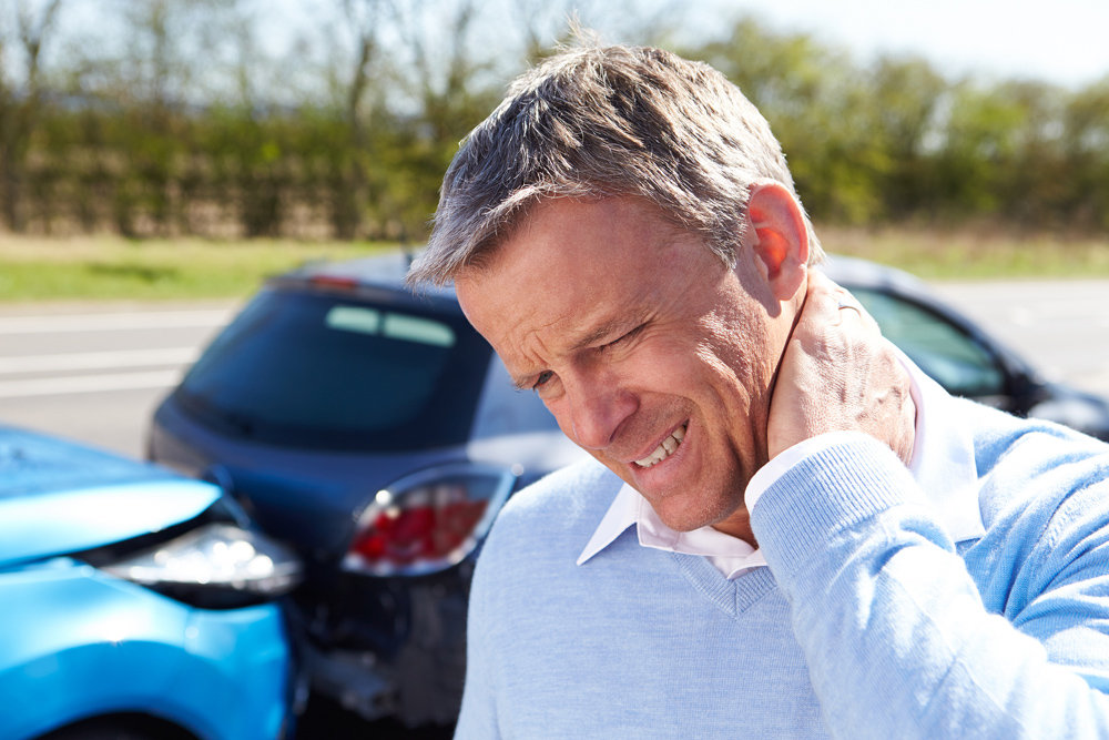 man holding neck because of whiplash pain with car accident in the background